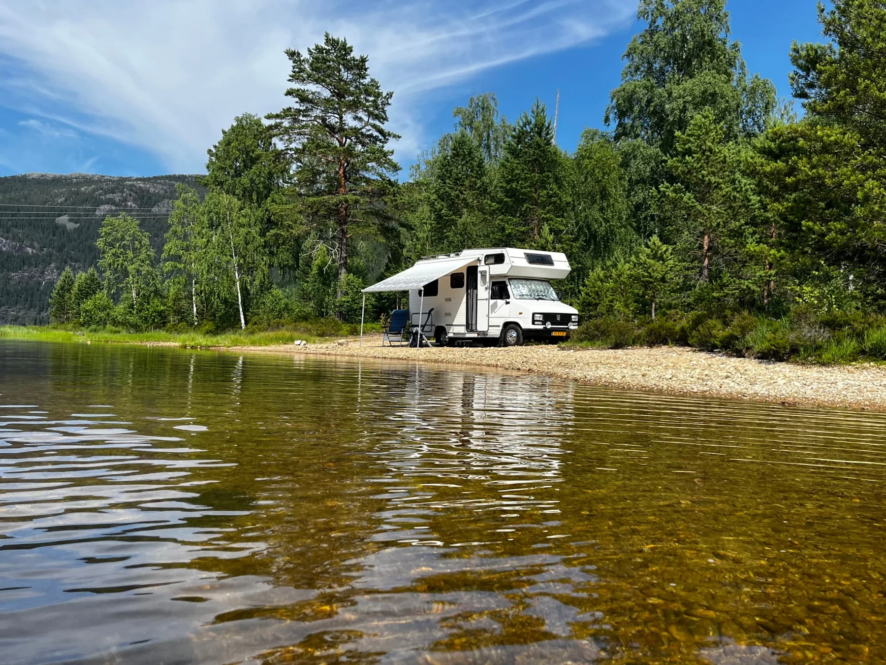 Witte camper aan een helder meer met bos en bergen
